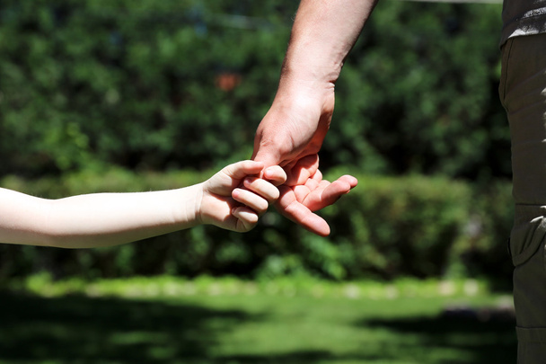 un padre sostiene la mano de un niño pequeño sobre un fondo verde
 - Foto, Imagen