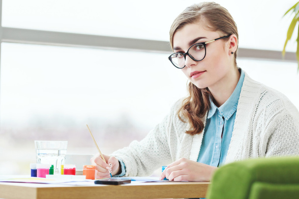 Chica con gafas sentado con pinturas de colores
 - Foto, imagen