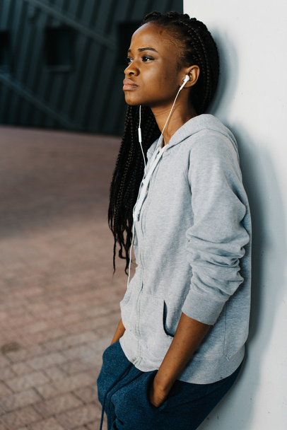 Young woman wearing earphones standing leaning a wall looking away confidently - Foto, Imagen