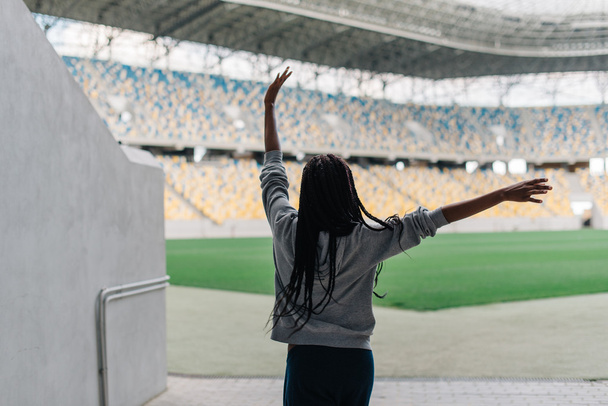 Back of african american woman standing among empty stadium celebrating, her arms raised punching the air with hands - Foto, Bild