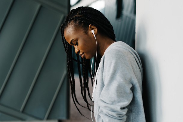Half-length close-up portrait of excited young African girl wearing hoodie and cool earphones standing looking down - Zdjęcie, obraz