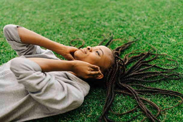 草の上に横たわる笑顔のアフリカ人女性の上からクローズアップ肖像画、側面図 - 写真・画像