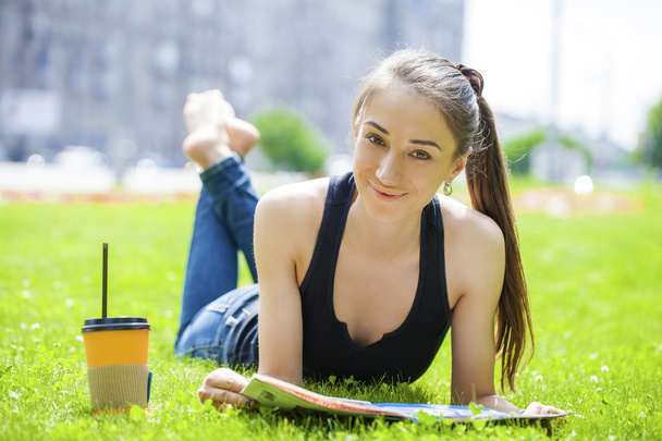 Young woman reading magazine lying on grass - Foto, afbeelding