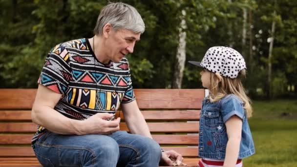 Dziadek, spędzać czas z jej wnuczka na ławce w parku - Materiał filmowy, wideo