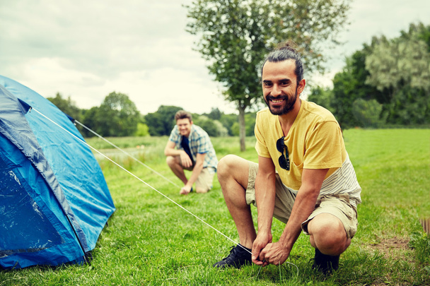smiling friends setting up tent outdoors - 写真・画像