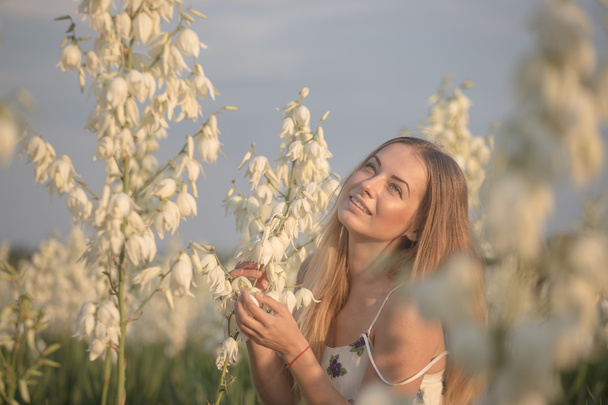 Prinsessa. Nuori kaunis kaunis nainen poseeraa pitkä ilta ylellinen mekko vastaan pensaita valkoisia kukkia
 - Valokuva, kuva