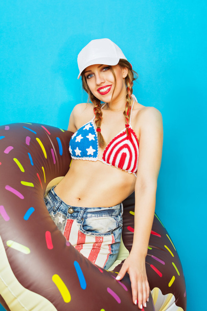 Cool young woman in American flag bikini with inflatable donut float - Фото, изображение