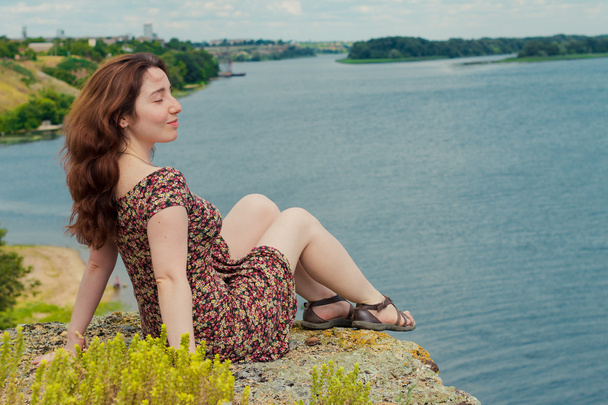 beautiful girl dreamily sits on the bank of the river - Photo, Image
