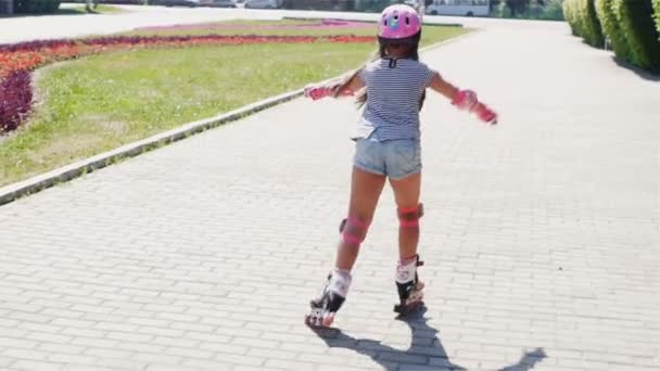 Parte posterior de la chica en casco rosa a caballo en patines en el parque de verano
 - Metraje, vídeo