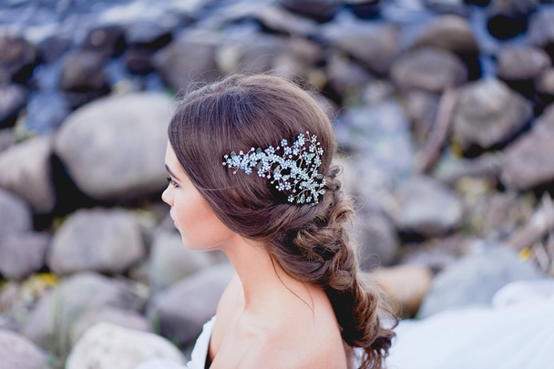 Gorgeous brunette European type sits in profile on the beach, looking romantically into the distance. Beautiful hair decoration handmade - Fotografie, Obrázek