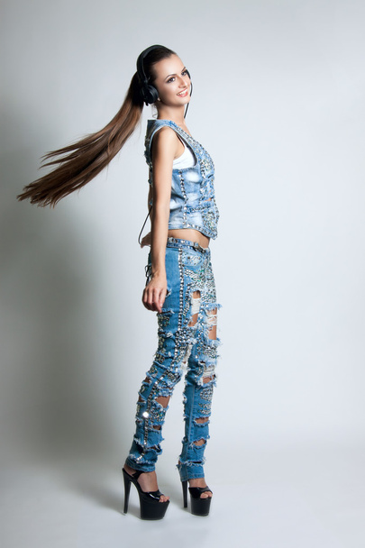 fashion portrait of a young beautiful girl. Girl with headphones in torn jeans posing in studio. Long hair. Denim with Rhinestones - Fotografie, Obrázek