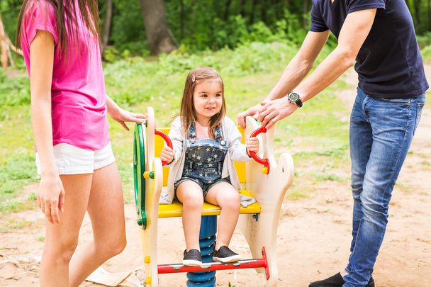 Дитяча дівчинка з батьками грає на дитячому майданчику в парку
 - Фото, зображення