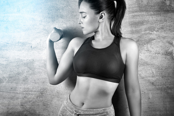 Fitte Frau beim Training mit Gewichten auf dem Hintergrund einer Betonwand in der Turnhalle. Konzept eines gesunden Lebensstils. - Foto, Bild