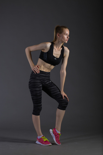Body of slim female in activewear doing posin on gray low key, perfect blonde - Photo, image