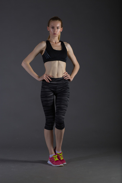 Body of slim female in activewear doing posin on gray low key, perfect blonde - Photo, Image