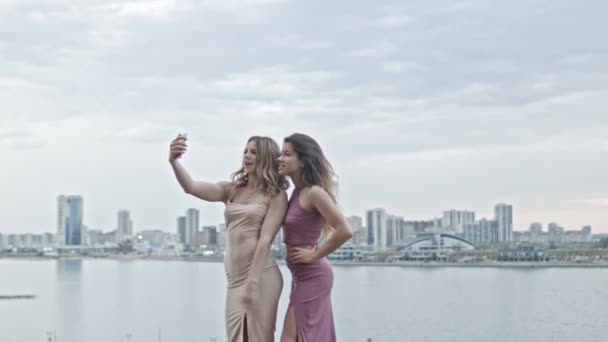 Dwóch atrakcyjnych młodych kobiet w sukienek na wysokim wzgórzu dostać autoportret za pomocą smartfonów, szeroko strzał - Materiał filmowy, wideo