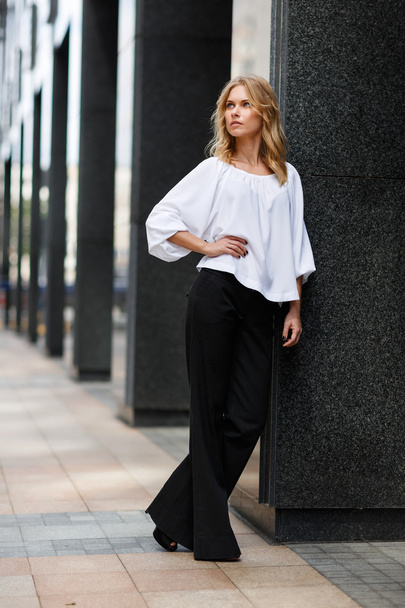 Blond woman in white blouse and black trousers near building - Fotografie, Obrázek