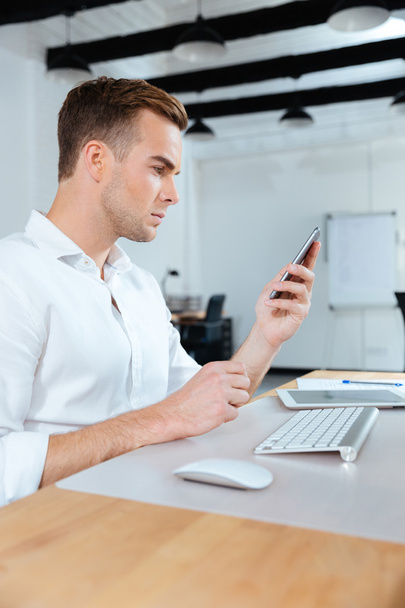 Homme d'affaires assis sur le lieu de travail et utilisant un téléphone portable
 - Photo, image