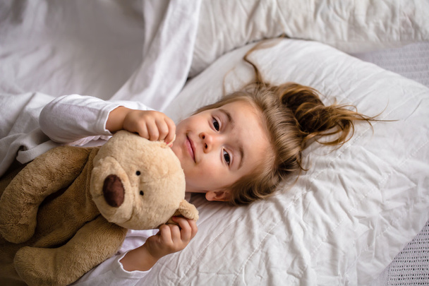 маленька дівчинка в ліжку з м'якою іграшкою емоції дитини
 - Фото, зображення