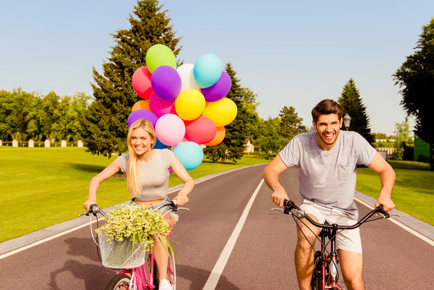 Happy couple in love riding a bicycle race with balloons in park - Foto, Imagen