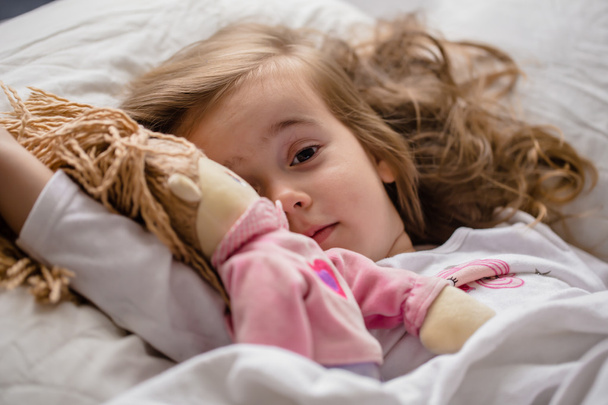 küçük kız yumuşak bez bebek beyaz yatakta uyuya kalır - Fotoğraf, Görsel
