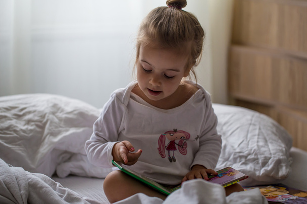 little girl reads a children's book in bed after sleep - Photo, Image