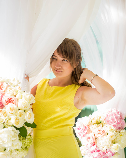 mooi jong meisje in een gele jurk op het terras van de achtergrond van verse bloemen - Foto, afbeelding