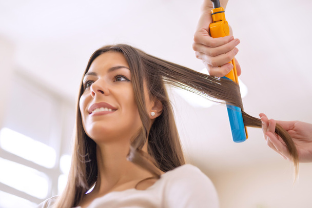 junge Frau sitzt, während der Friseur ihr Haar frisiert - Foto, Bild