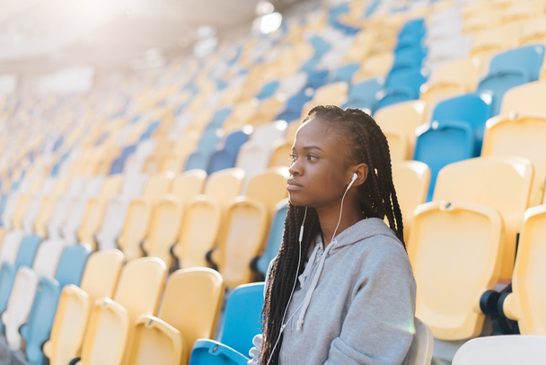 Charming african american woman in gray sportswear on bleachers waiting for a show, celebration - Valokuva, kuva