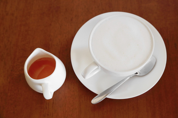 Een kopje warme koffie met melk schuim en honing op houten achtergrond - Foto, afbeelding