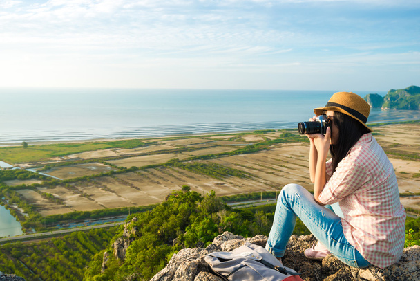 Aasialainen hipster tyttö istuu vuoren huipulla kameran kanssa
. - Valokuva, kuva