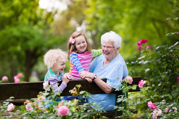 Бабушка и дети сидят в розовом саду
 - Фото, изображение