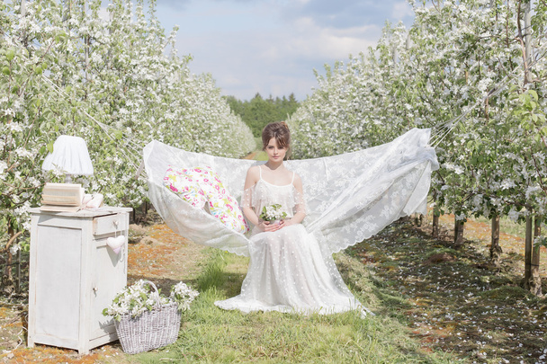 beautiful sexy cute girl in a light white dress in apple blossoming garden sees on the hammock with a book - Fotografie, Obrázek