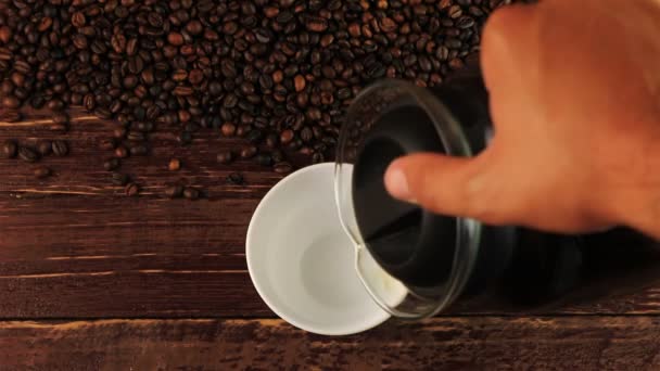Pouring coffee into white cup and coffee beans on brown wooden table - Footage, Video