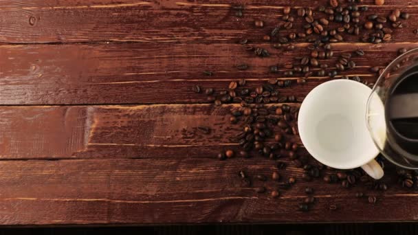 Koffie gieten in witte kop en koffiebonen op bruin houten tafel - Video