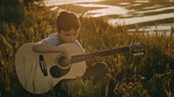 Chłopiec w lato pole szkolenia się grać na gitarze o zachodzie słońca latem, na wysokim wzgórzu - Materiał filmowy, wideo