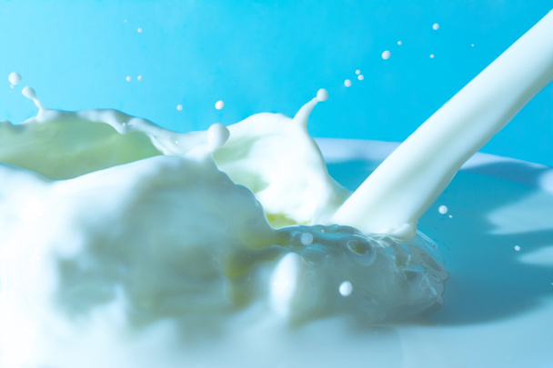 Splashes of milk on the surface of the milk on a light blue background - Fotoğraf, Görsel
