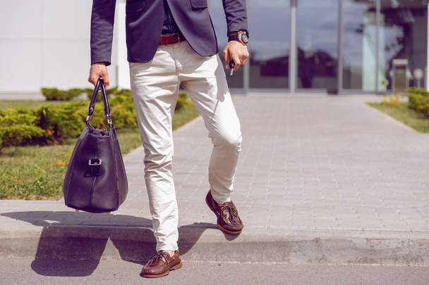 hombre de negocios vestido a la moda camina desde el edificio de oficinas con una bolsa y llaves del coche en la mano
. - Foto, Imagen