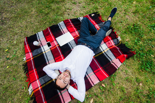 Happy young man with laptop relaxing on the grass, view from the top - Photo, Image