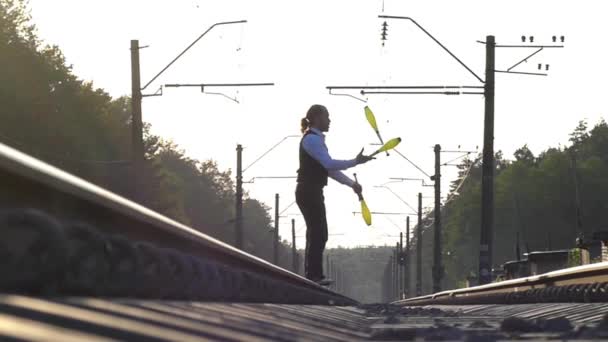 Un tipo haciendo malabares en las vías del tren. A cámara lenta. Puesta de sol. Equilibrio del ferrocarril
. - Metraje, vídeo