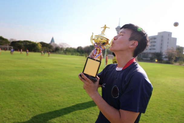 asiatischer Fußballer Mann küsst Trophäe, feiert seinen Sieger Meister des Fußballsports Spiel auf der grünen Wiese.  - Foto, Bild
