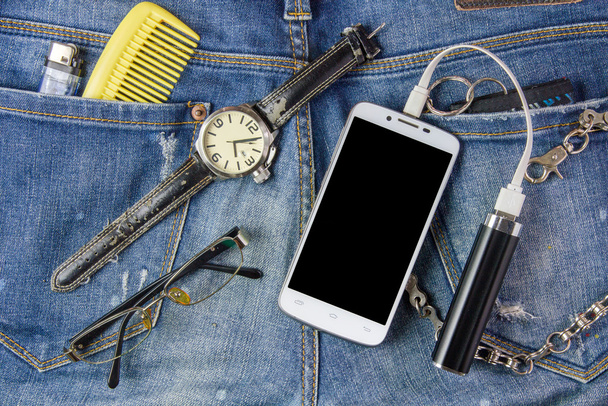 Smart phone, lunettes, batterie portable et regarder sur jeans bac
 - Photo, image