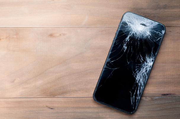 Smartphone mobile with a broken screen. Background wood - Photo, Image