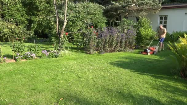 Miespuolinen puutarhuri, joka leikkaa nurmikkoa talonsa pihalla. 4K
 - Materiaali, video