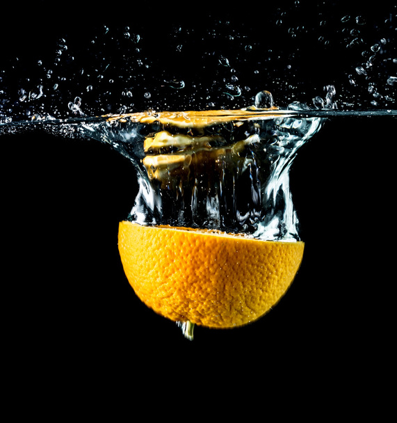 Orange slices falling into the water close-up, macro, splash, bubbles, black background - Photo, image