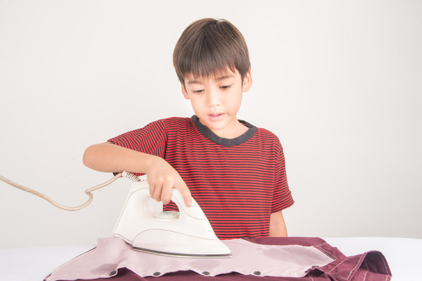 Мальчик гладит свою одежду, помогая домашним работам.
 - Фото, изображение