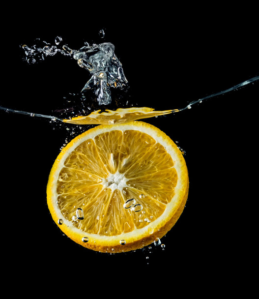 Orange slices falling into the water close-up, macro, splash, bubbles, black background - Fotó, kép