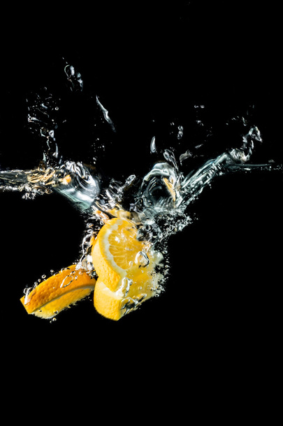 Orange slices falling into the water close-up, macro, splash, bubbles, black background - Photo, Image