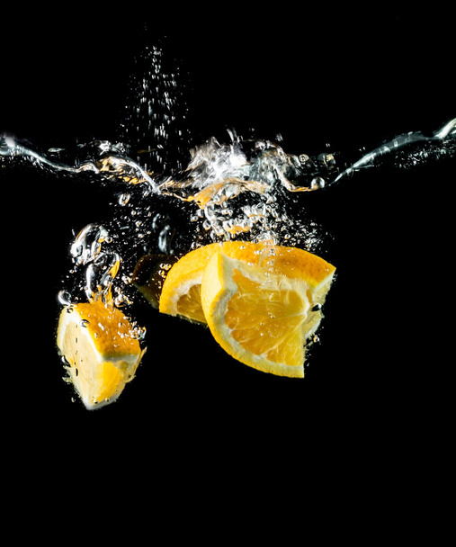 Orangenscheiben, die in Nahaufnahme ins Wasser fallen, Makro, Spritzer, Blasen, schwarzer Hintergrund - Foto, Bild