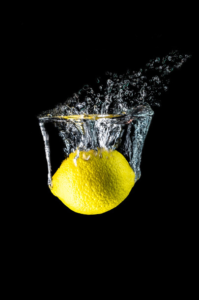 Lemon falling into the water close-up, macro, splash, bubbles, isolated on black  - Valokuva, kuva